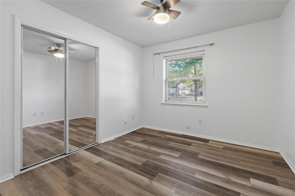 Room featuring wood-finish flooring, sliding mirrored closet doors, a single-hung window, and a ceiling fan with integrated light fixture