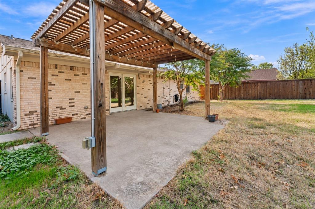 Backyard patio featuring a wood-beam pergola, concrete flooring, brick exterior siding, and a wooden privacy fence