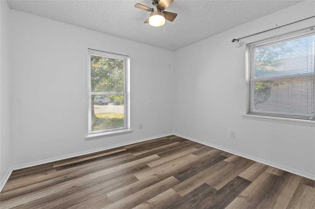 Room featuring wood-finish flooring, two windows with horizontal blinds, and a ceiling-mounted light fixture with fan blades