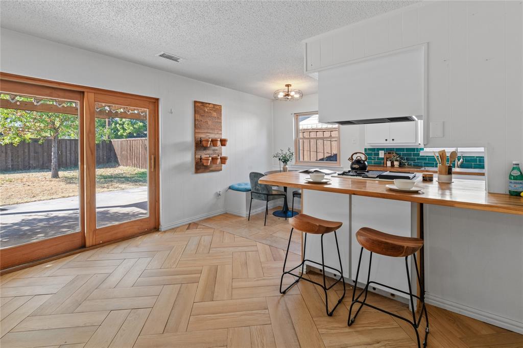 Herringbone-pattern wood-finish flooring, breakfast bar with wood countertop, teal tile backsplash, and wooden-frame sliding glass door Herringbone-pattern wood-finish flooring, breakfast bar with wood countertop, teal tile backsplash, and wooden-frame sliding glass door
