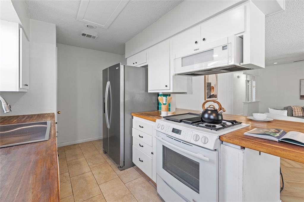 Kitchen featuring white cabinetry, wood-finish countertops, tile flooring, and stainless steel appliances