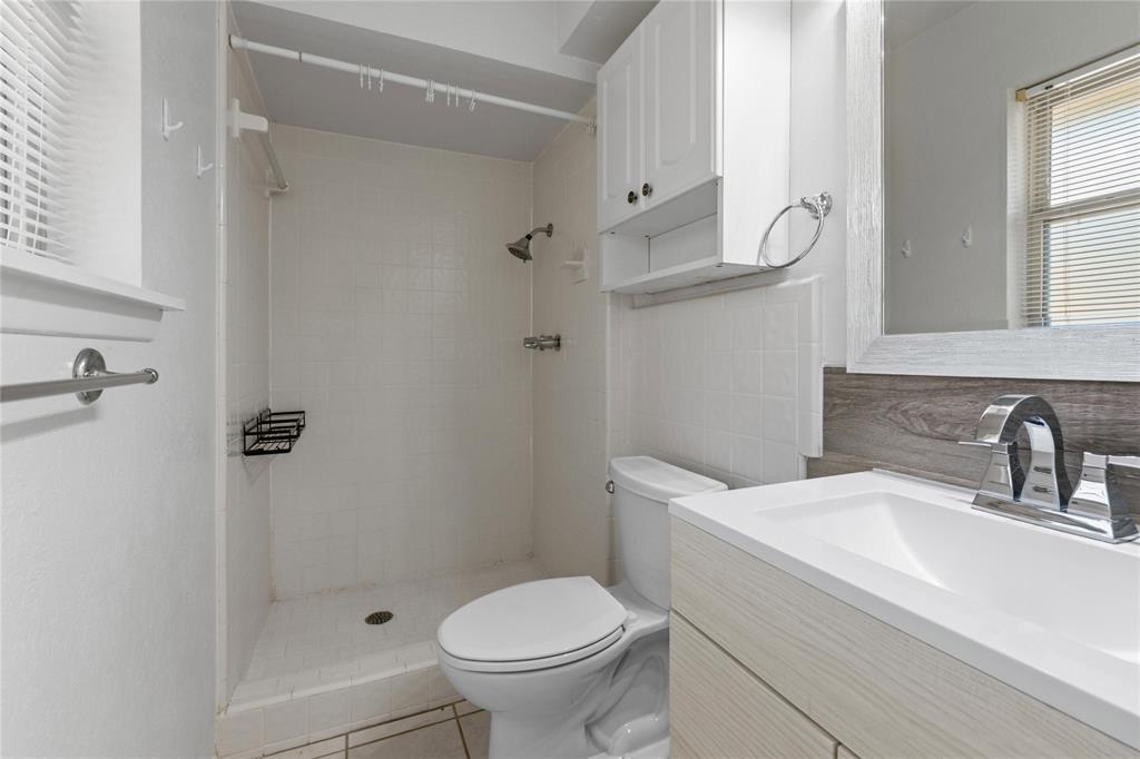 Bathroom featuring a wood-finish vanity with a rectangular sink, chrome fixtures, tiled shower enclosure, and built-in upper cabinetry