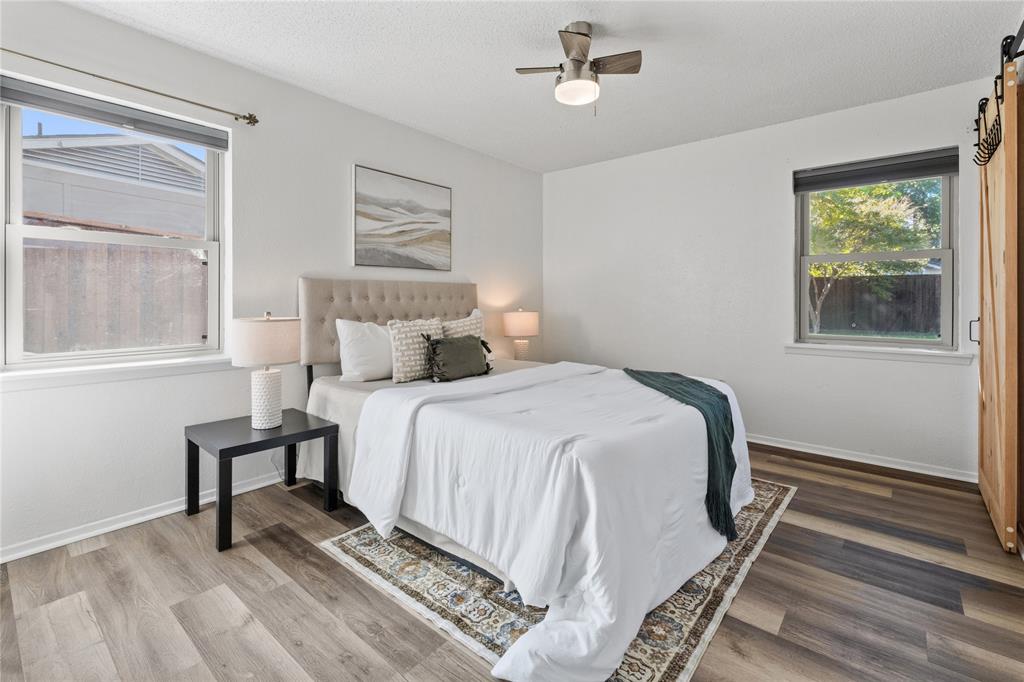 Bedroom with wood-finish flooring, dual windows with roller shades, a ceiling fan with integrated lighting, and a sliding barn-style door
