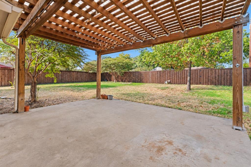 Covered patio featuring a wooden pergola, concrete flooring, and a fenced backyard with mature trees