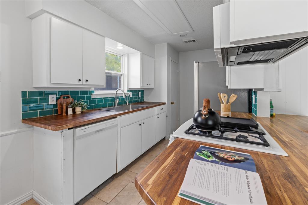 Kitchen featuring wood-finish countertops, white cabinetry, a deep teal subway tile backsplash, a stainless steel sink, and a built-in gas cooktop