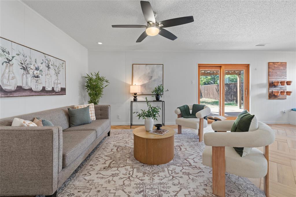 Living area featuring wood-finish flooring in a herringbone pattern, a central ceiling fan with integrated lighting, and wooden-framed glass sliding doors Living area featuring wood-finish flooring in a herringbone pattern, a central ceiling fan with integrated lighting, and wooden-framed glass sliding doors