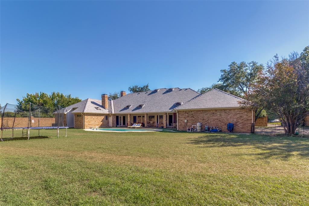 Expansive backyard featuring a brick exterior, a covered patio, an in-ground swimming pool, and mature trees