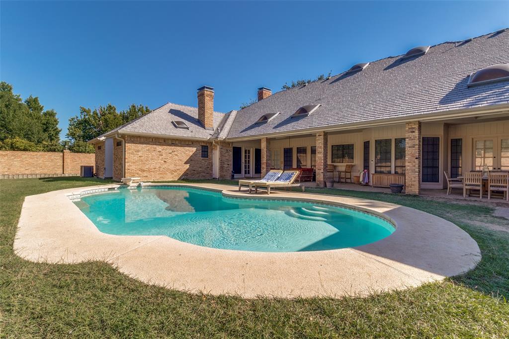 In-ground pool with stone-texture decking, covered patio area, brick exterior, multiple skylights, and a high-pitched roofline