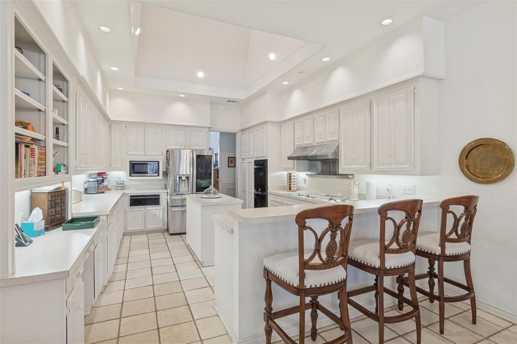 Kitchen featuring white cabinetry, central island with prep sink, recessed ceiling lighting, tile flooring, and integrated stainless steel appliances