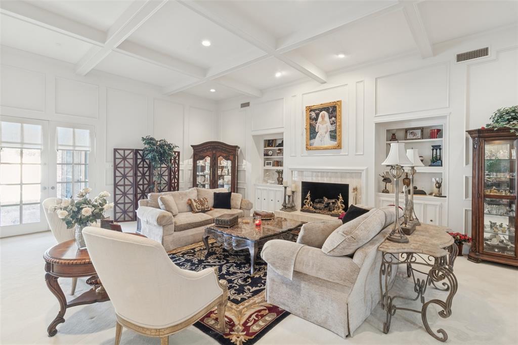 Coffered ceiling, custom wall paneling, built-in shelving, fireplace with decorative surround, and multi-pane glass doors
