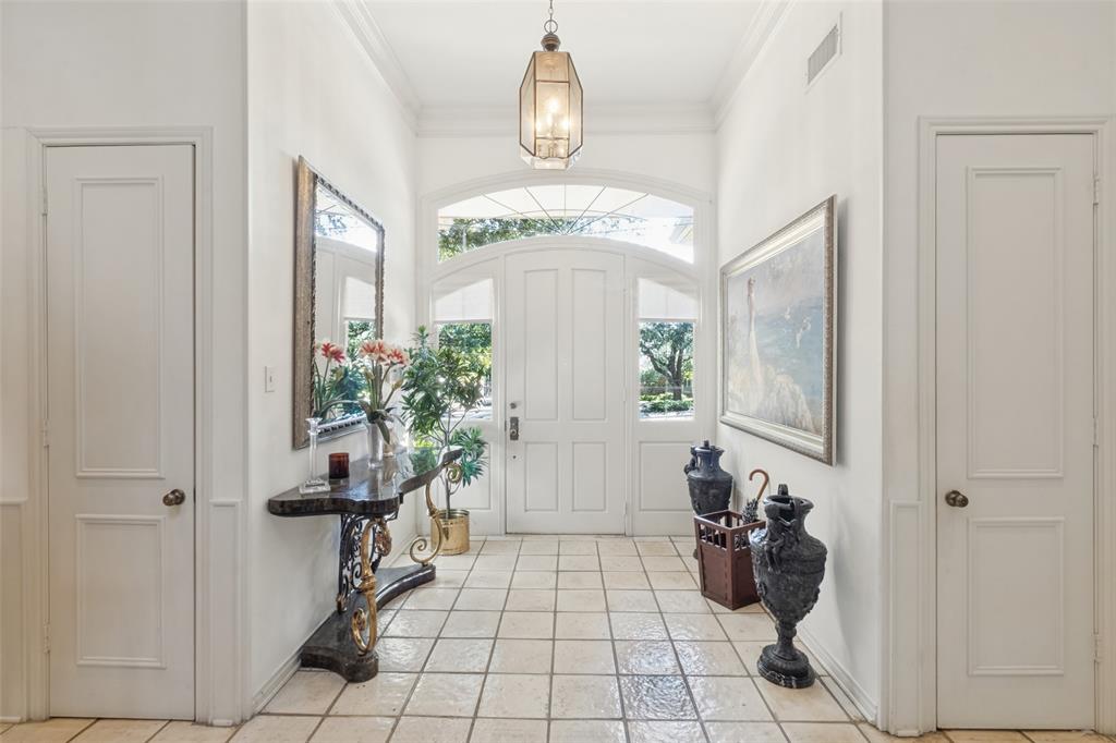 Foyer featuring a high ceiling, ceramic tile flooring, a multi-paneled door with a glass arched transom, and a hanging metal pendant fixture
