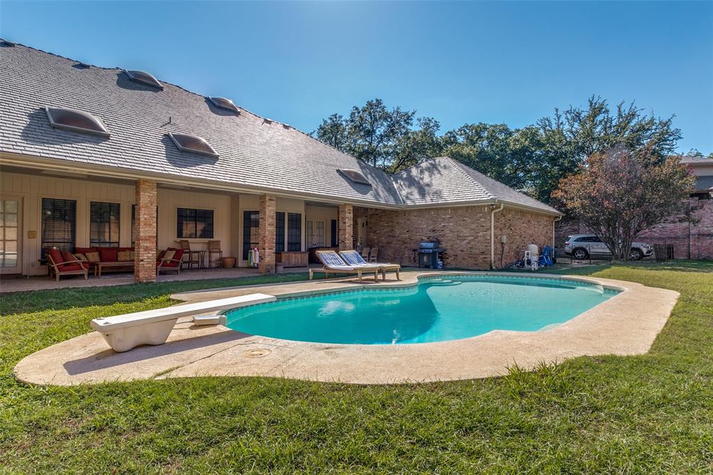 Backyard featuring a swimming pool with a diving board, a covered patio with brick columns, and multiple roof-mounted skylights
