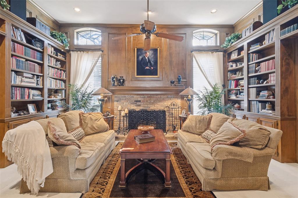 Custom floor-to-ceiling wood cabinetry, expansive built-in bookshelves, brick fireplace surround with heavy mantel, recessed lighting, and dual arched windows