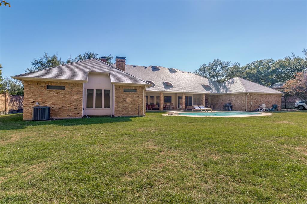 Brick exterior residence featuring a sprawling lawn, a rear covered patio, an in-ground swimming pool, and roof-integrated skylights