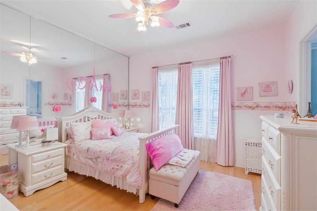 Spacious room featuring wood-finish flooring, full-wall mirrors, dual windows with plantation shutters, and a ceiling fan with integrated lighting