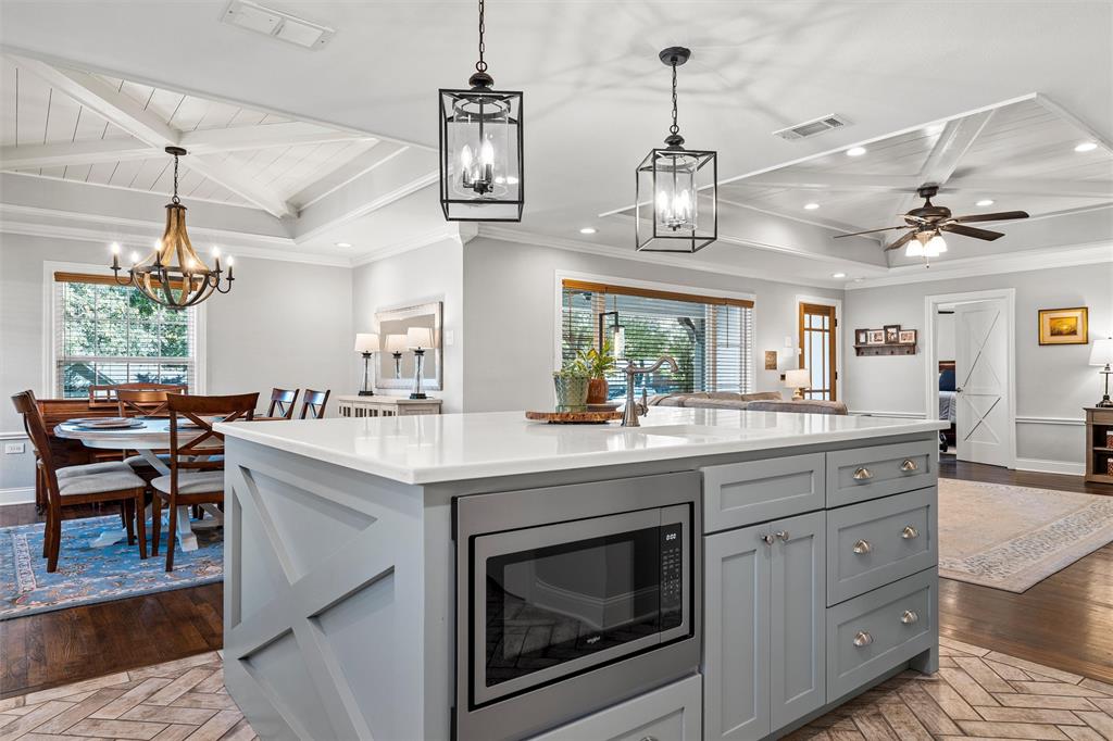 Center island featuring a stone-surface countertop, built-in microwave, and x-pattern cabinetry, complemented by overhead lantern-style pendant lighting and coffered ceilings