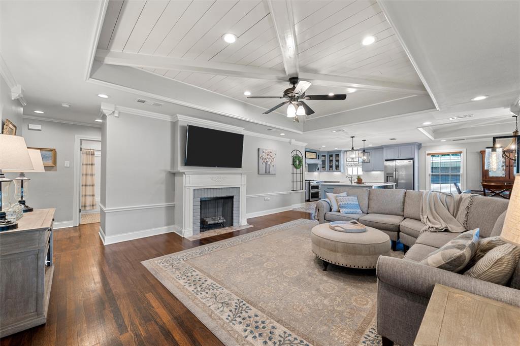 Tray ceiling with wood-plank detailing and exposed beams, wood-finish flooring, and a fireplace with a custom mantel surround
