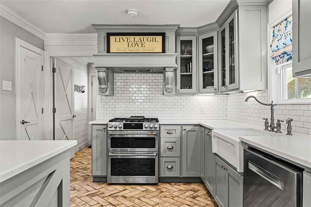 Kitchen featuring gray shaker-style cabinetry, white subway tile backsplash, stainless steel gas range with a custom range hood, farmhouse sink, and herringbone-patterned brick flooring