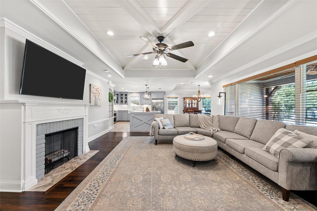 Vaulted ceiling with cross-beam detailing, fireplace with a custom-painted brick surround, recessed lighting, ceiling fan, and wood-finish flooring