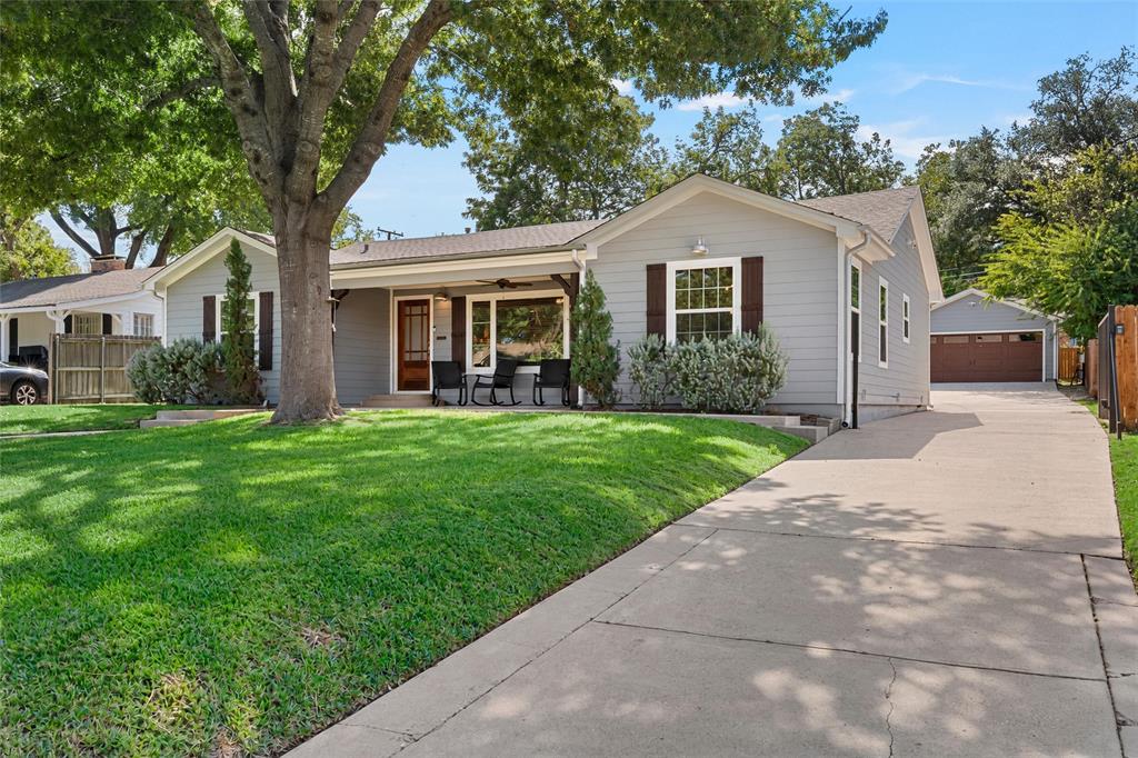 Single-story exterior featuring lap siding, dark shutter accents, a covered front porch, mature landscaping, and a detached two-car garage