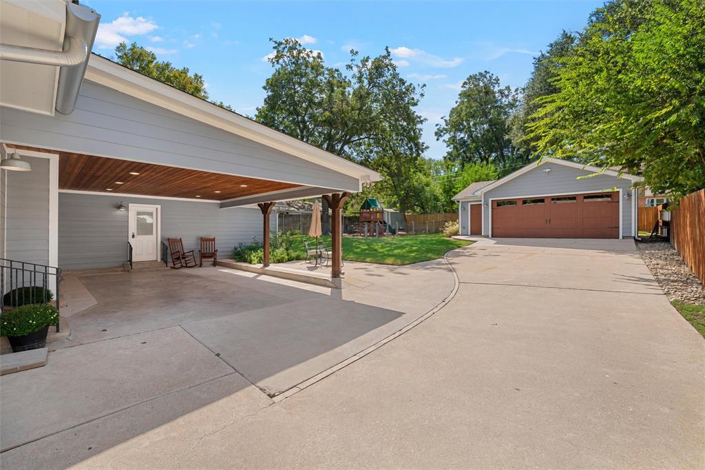 Covered carport with wood-plank ceiling, detached multi-car garage, concrete driveway, and backyard green space