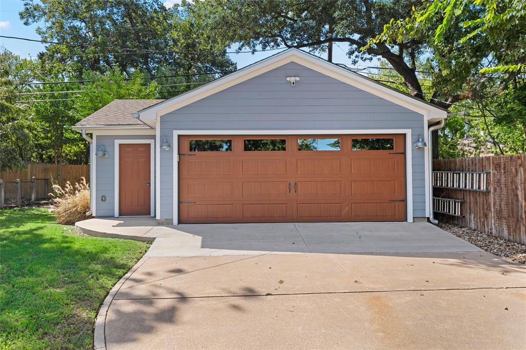 Detached garage featuring horizontal lap siding, a paneled garage door with glass inserts, a separate service door, and exterior wall-mounted lighting