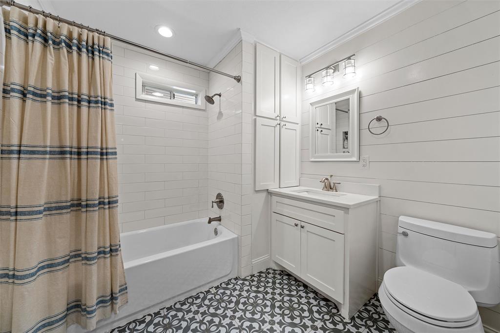 Bathroom featuring horizontal shiplap walls, patterned tile flooring, white shaker-style vanity with a built-in linen cabinet, and white subway tile shower surround