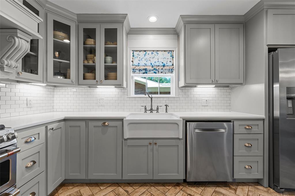 Kitchen featuring gray shaker-style cabinetry with glass-front uppers, white subway tile backsplash, farmhouse-style apron sink, and herringbone-patterned flooring