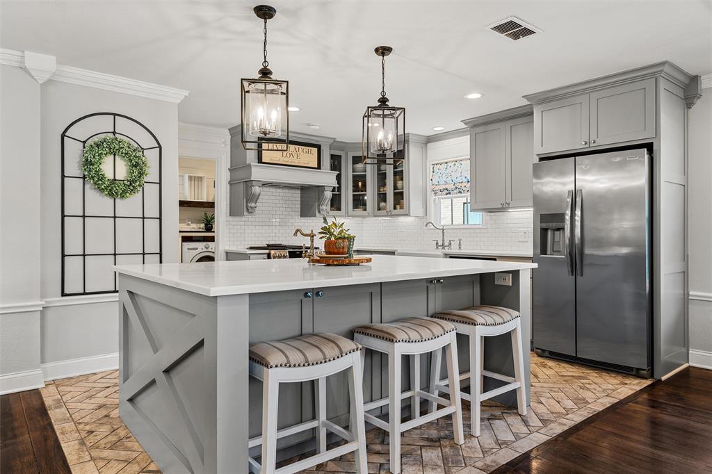 Kitchen featuring a central island with a solid surface countertop, herringbone-patterned flooring, cabinetry with crown molding, stainless steel refrigerator, and hanging pendant lanterns