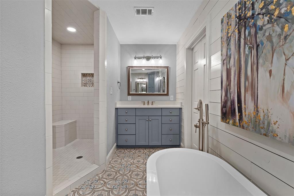 Bathroom featuring a freestanding tub, walk-in shower with built-in seating, dual-tone vanity cabinet, patterned floor tile, and horizontal wall paneling