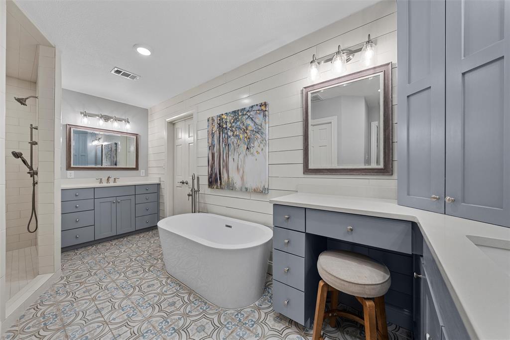 Freestanding soaking tub, dual-sink vanity with light-colored countertops, shiplap wall accents, patterned tile flooring, and walk-in shower with vertical tile surround
