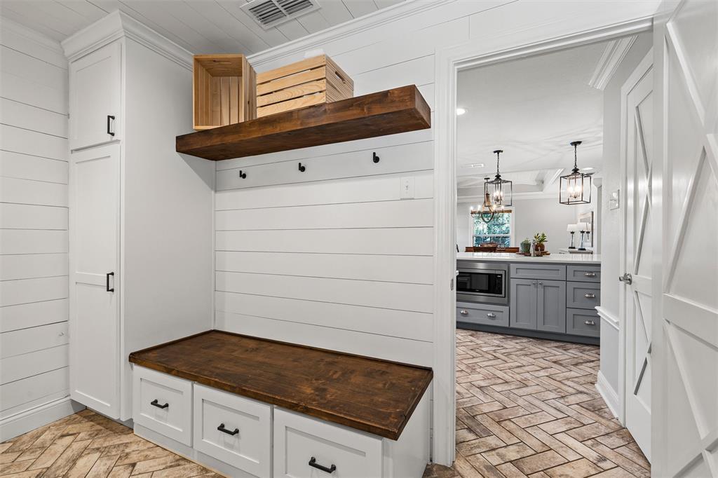 Custom built-in mudroom bench with a wood-finish top and lower storage drawers, white shiplap wall paneling, stained wood floating shelf, tall floor-to-ceiling cabinetry, and herringbone-patterned flooring