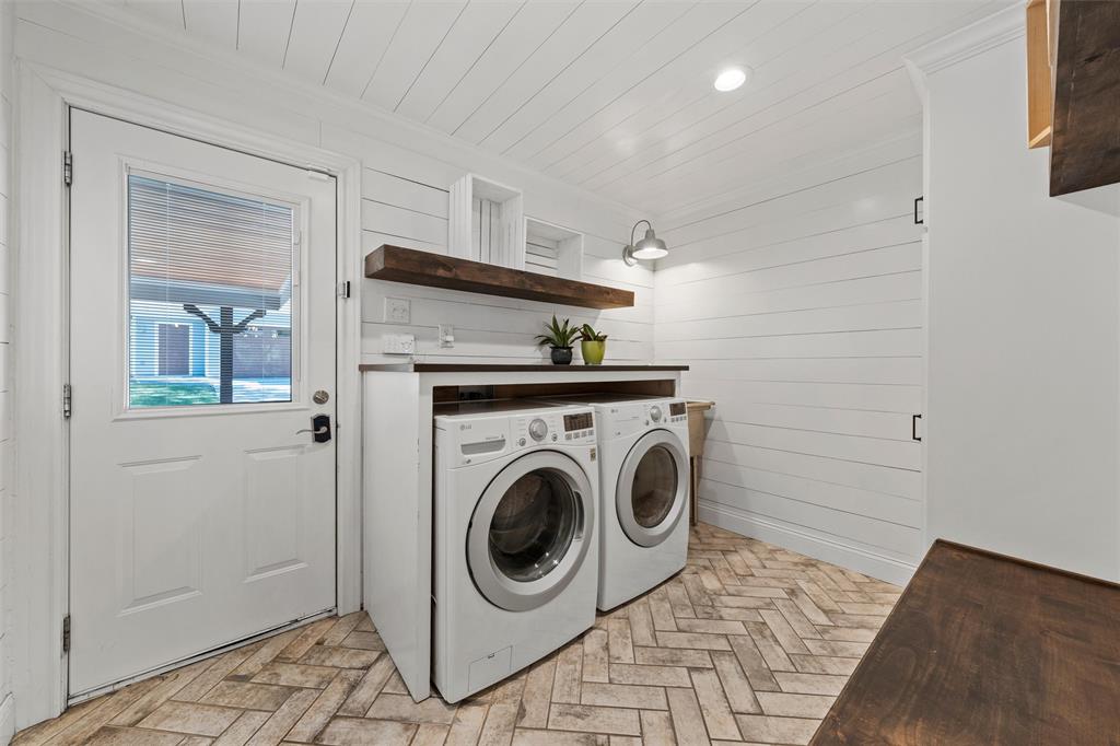 Laundry room featuring herringbone-patterned tile flooring, horizontal plank walls, a built-in wood countertop, wall-mounted gooseneck lighting, and a solid-core exterior door with an inset glass pane