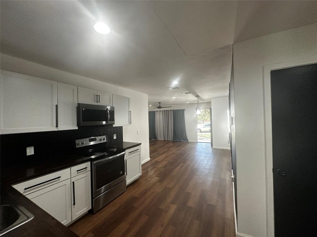 Kitchen featuring white shaker-style cabinetry, dark countertops, a stainless steel range and microwave, and wood-finish flooring Kitchen featuring white shaker-style cabinetry, dark countertops, a stainless steel range and microwave, and wood-finish flooring