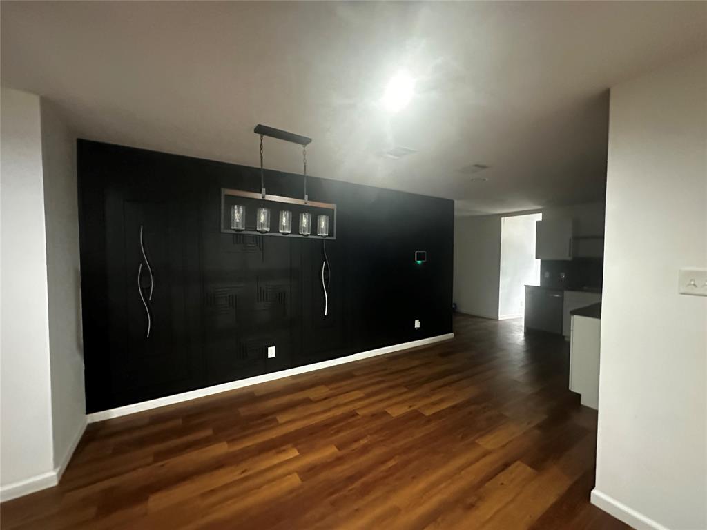 Wood-finish flooring, accent wall with textured detailing, and a modern five-light rectangular chandelier Wood-finish flooring, accent wall with textured detailing, and a modern five-light rectangular chandelier