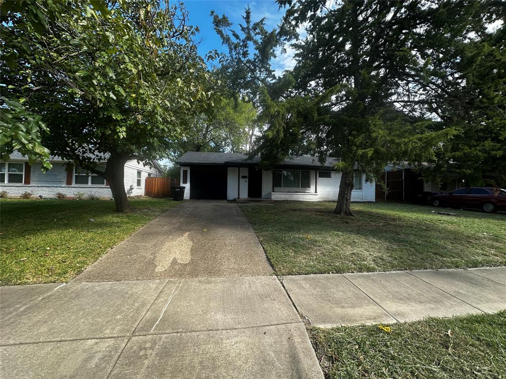 Single-story residence featuring a painted masonry exterior, attached garage, concrete driveway, and mature trees