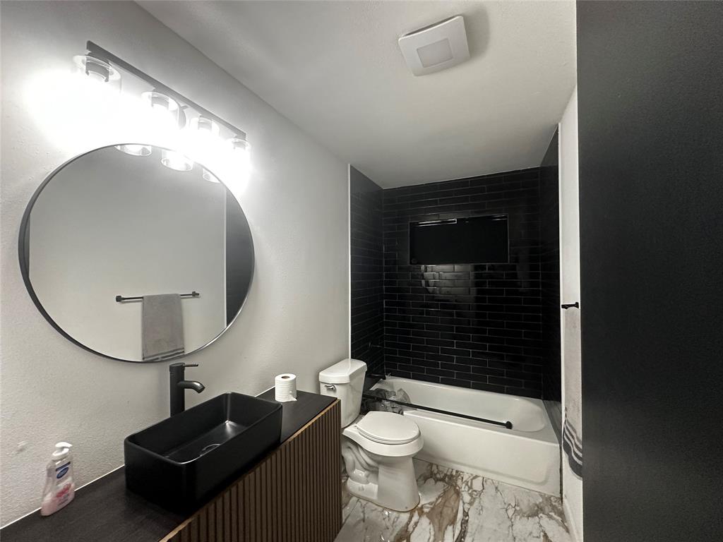 Modern vanity with vertical slat detailing, rectangular vessel sink, matte black faucet, circular wall mirror, and tub enclosure with black subway tile surround