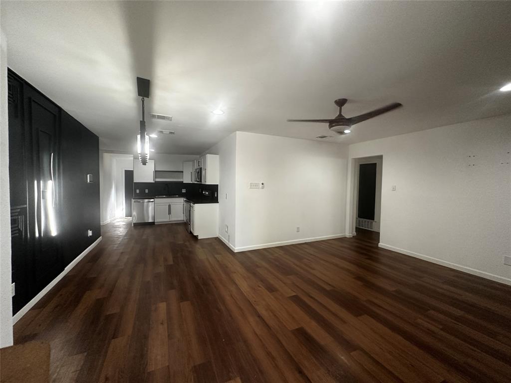 Open-concept interior featuring wood-finish flooring, a dark accent wall, a ceiling fan, recessed lighting, and a kitchen equipped with stainless steel appliances Open-concept interior featuring wood-finish flooring, a dark accent wall, a ceiling fan, recessed lighting, and a kitchen equipped with stainless steel appliances