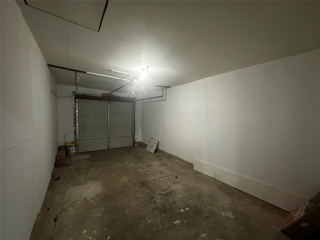Enclosed garage featuring a concrete floor, painted walls, and a sectional overhead door with an integrated automatic opener Enclosed garage featuring a concrete floor, painted walls, and a sectional overhead door with an integrated automatic opener