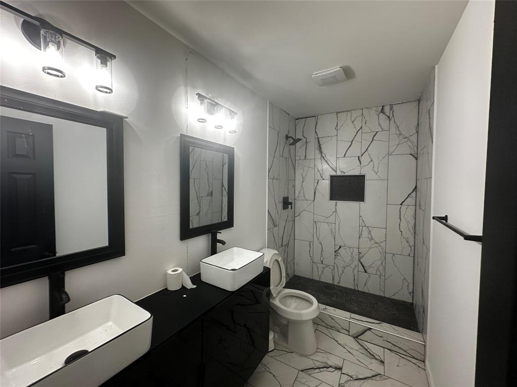Bathroom featuring a dual vanity with white vessel sinks, black matte hardware, framed mirrors, and a walk-in shower with veined tile surround and built-in niche