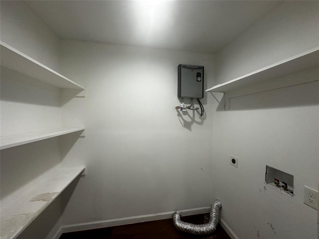 Storage area featuring three tiers of built-in shelving, wall-mounted water heater unit, and dedicated utility hookups Storage area featuring three tiers of built-in shelving, wall-mounted water heater unit, and dedicated utility hookups