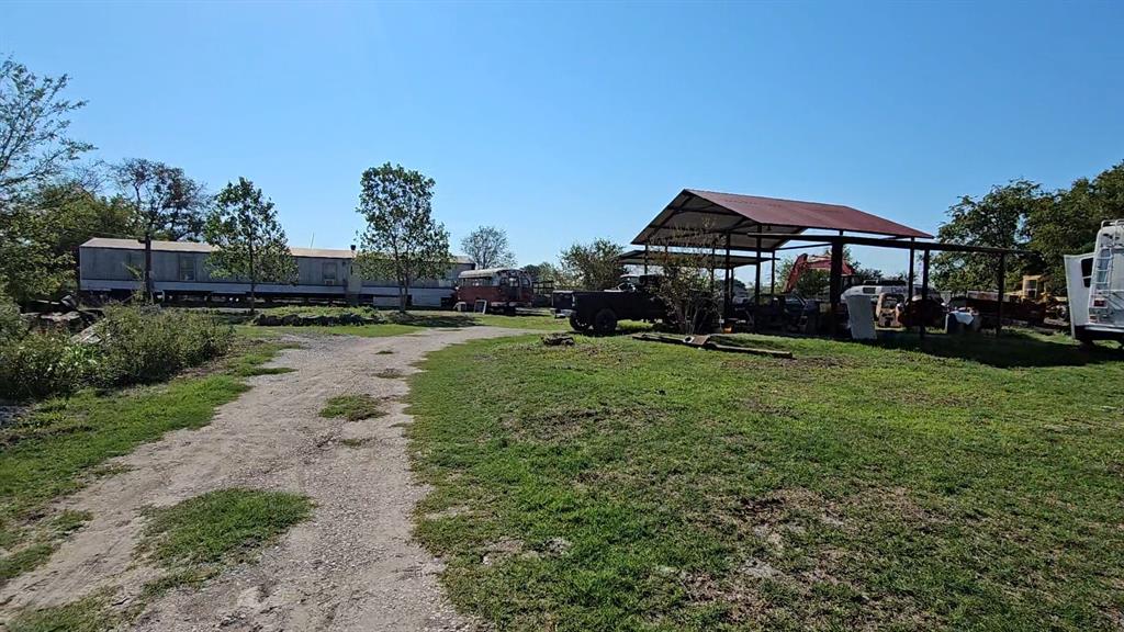 Expansive acreage featuring a gravel driveway, mature trees, and an open-sided metal structure with a gable roof