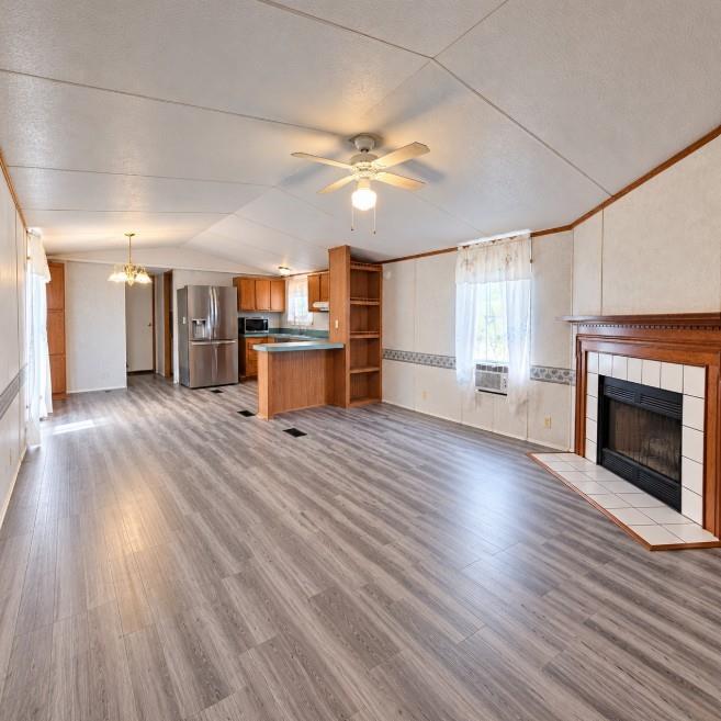 Wood-finish flooring, fireplace with a tile surround and wood mantel, built-in shelving, wood cabinetry, and a ceiling fan