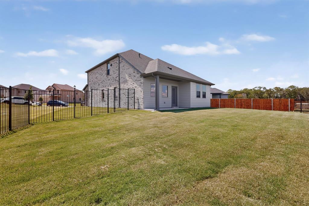 Rear exterior featuring a brick and siding facade, a covered patio, and a fenced-in lawn with metal and wood privacy fencing