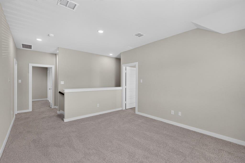 Interior space featuring neutral wall tones, wall-to-wall carpeting, recessed ceiling lighting, and a half-height partition wall with a dark handrail Interior space featuring neutral wall tones, wall-to-wall carpeting, recessed ceiling lighting, and a half-height partition wall with a dark handrail