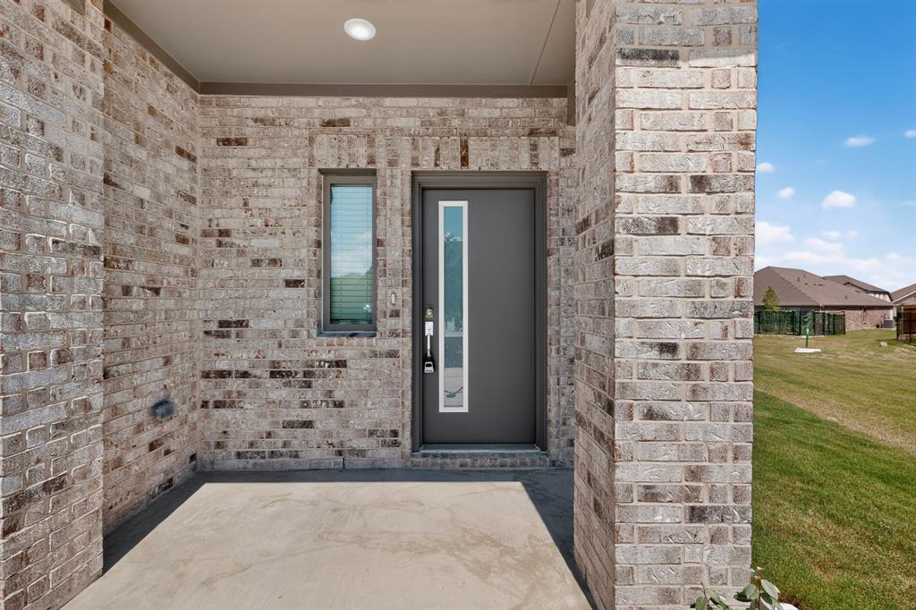 Covered entry featuring a brick facade, recessed lighting, and a modern door with a vertical glass pane Covered entry featuring a brick facade, recessed lighting, and a modern door with a vertical glass pane