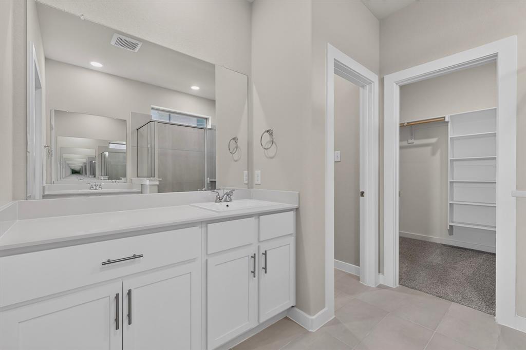 White vanity featuring shaker-style cabinetry, matte black hardware, and a solid-surface countertop with an integrated basin, complemented by a large wall-mounted mirror and built-in closet shelving