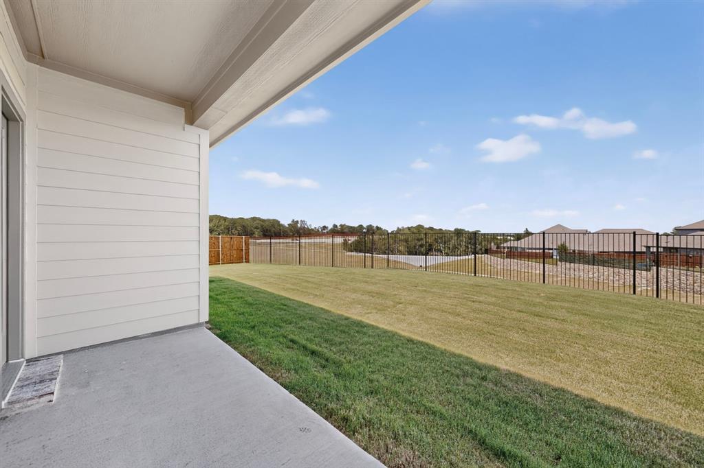 Covered concrete patio with horizontal siding, large grass lawn, and metal perimeter fencing