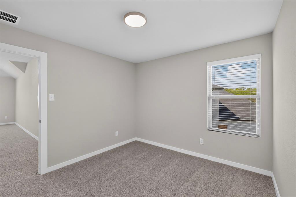 Neutral-toned interior space featuring wall-to-wall carpeting, a single window with horizontal blinds, and a flush-mount circular ceiling light