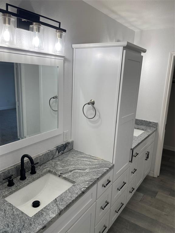 Bathroom vanity featuring white shaker-style cabinetry, stone-patterned countertops, undermount rectangular sinks, matte black widespread faucets, and a three-light fixture